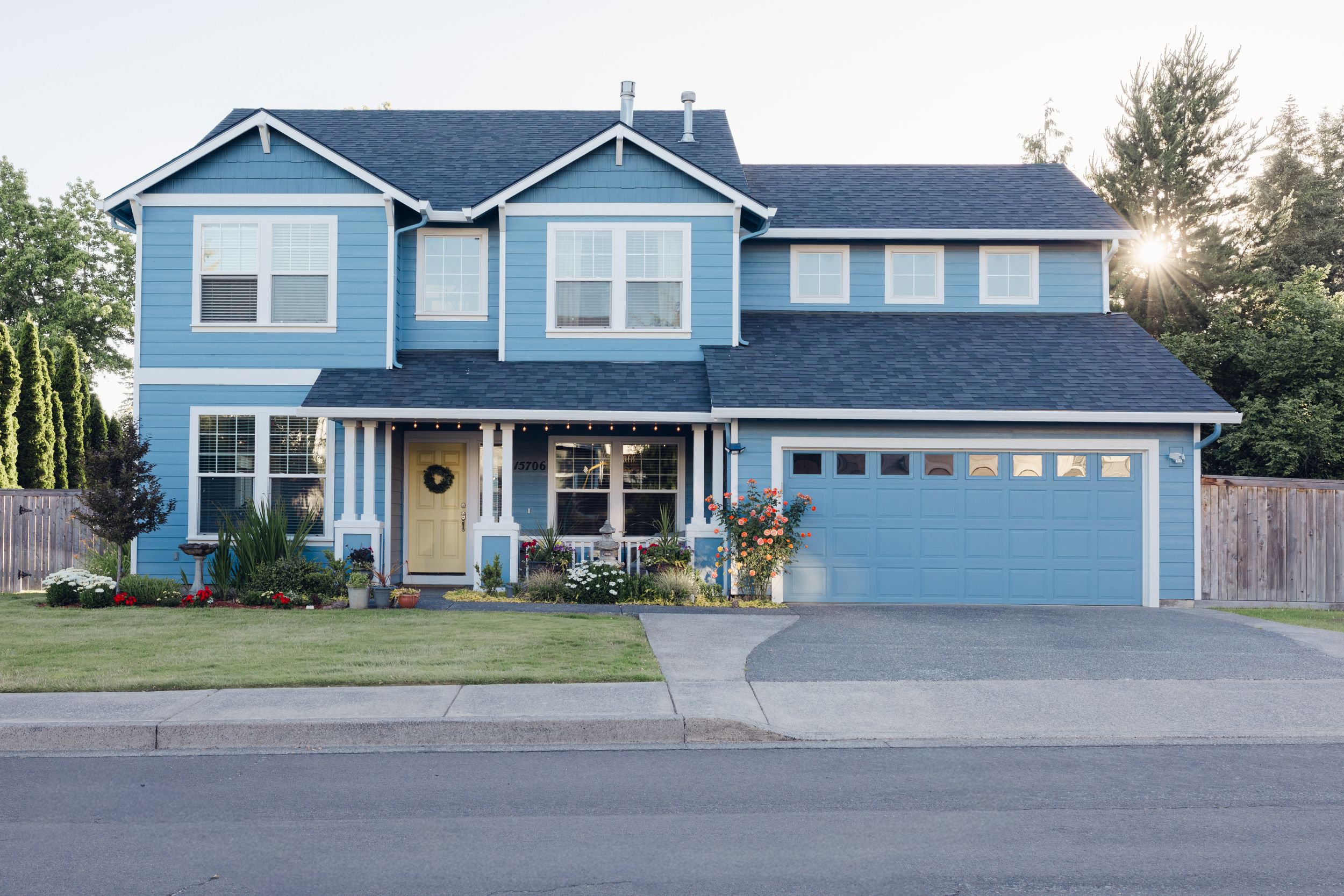 A two-story blue craftsman home with a two-car garage, covered porch, and well-manicured lawn on a quiet street.