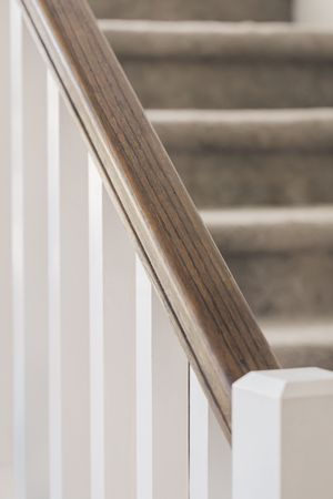 Close-up of a dark wood stair handrail with white balusters and carpeted steps in the background.