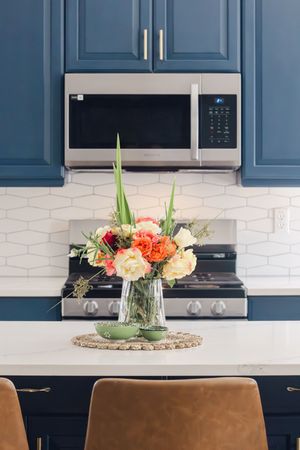 Tri-CitiModern kitchen with blue cabinets, stainless steel microwave and stove, white geometric backsplash, and colorful flower arrangement.