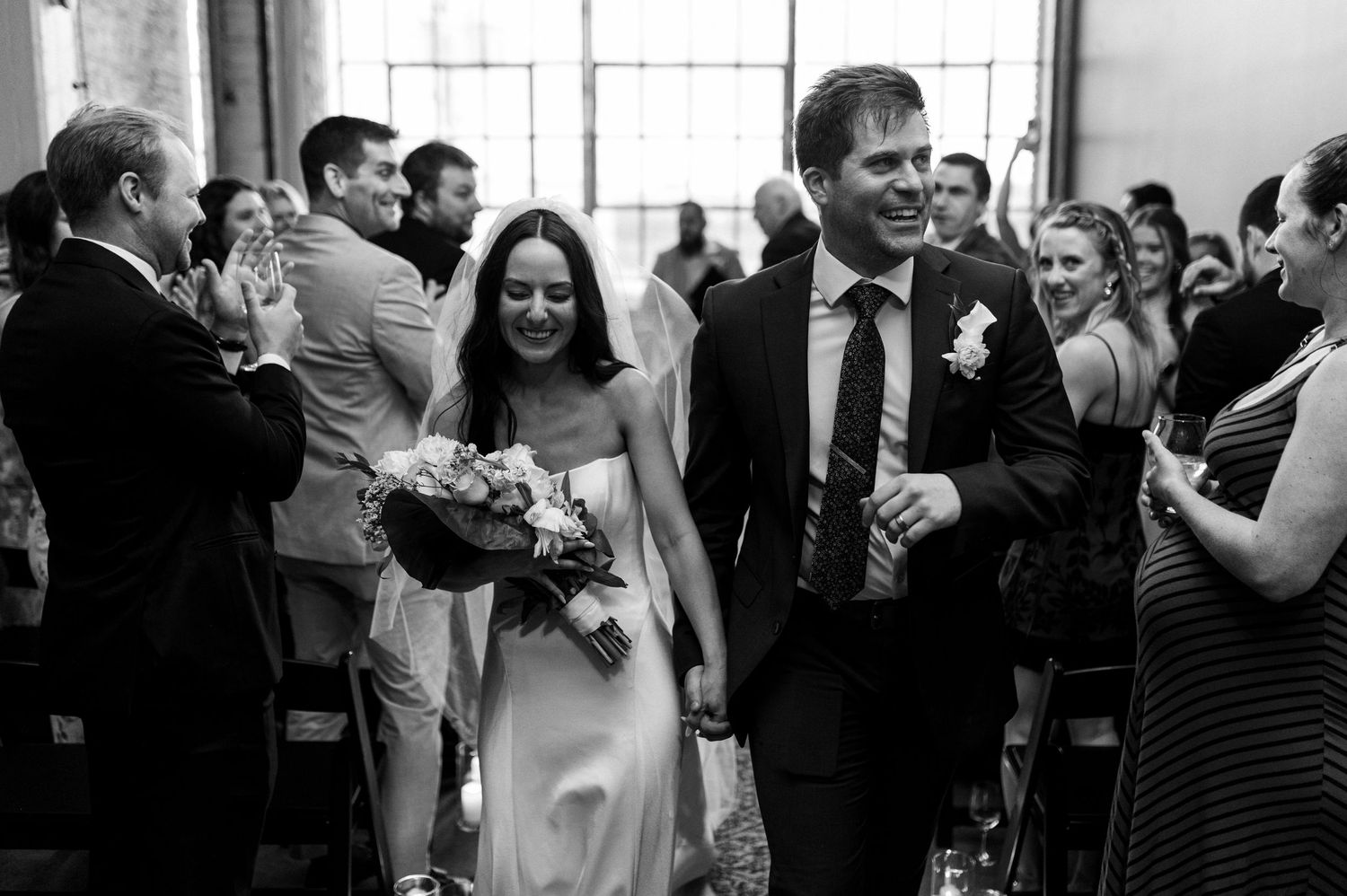 Black and white wedding reception photo of guests dancing with children, chandelier overhead, candid joyful moment.