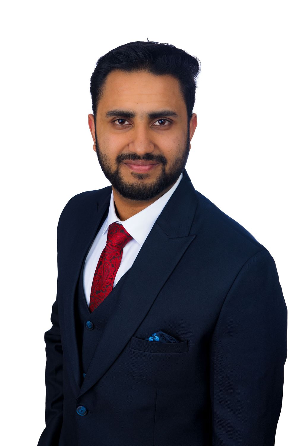 Professional man in navy suit with red tie and blue pocket square smiling against white background.