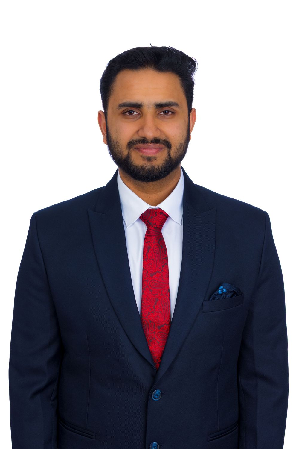 Professional man in navy suit with red tie and pocket square smiling against white background.