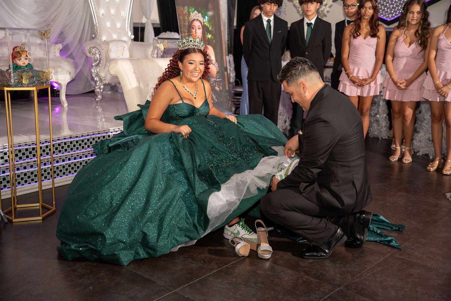 A quinceañera ceremony with a girl in a green ballgown receiving her crown from a woman in a gold gown.