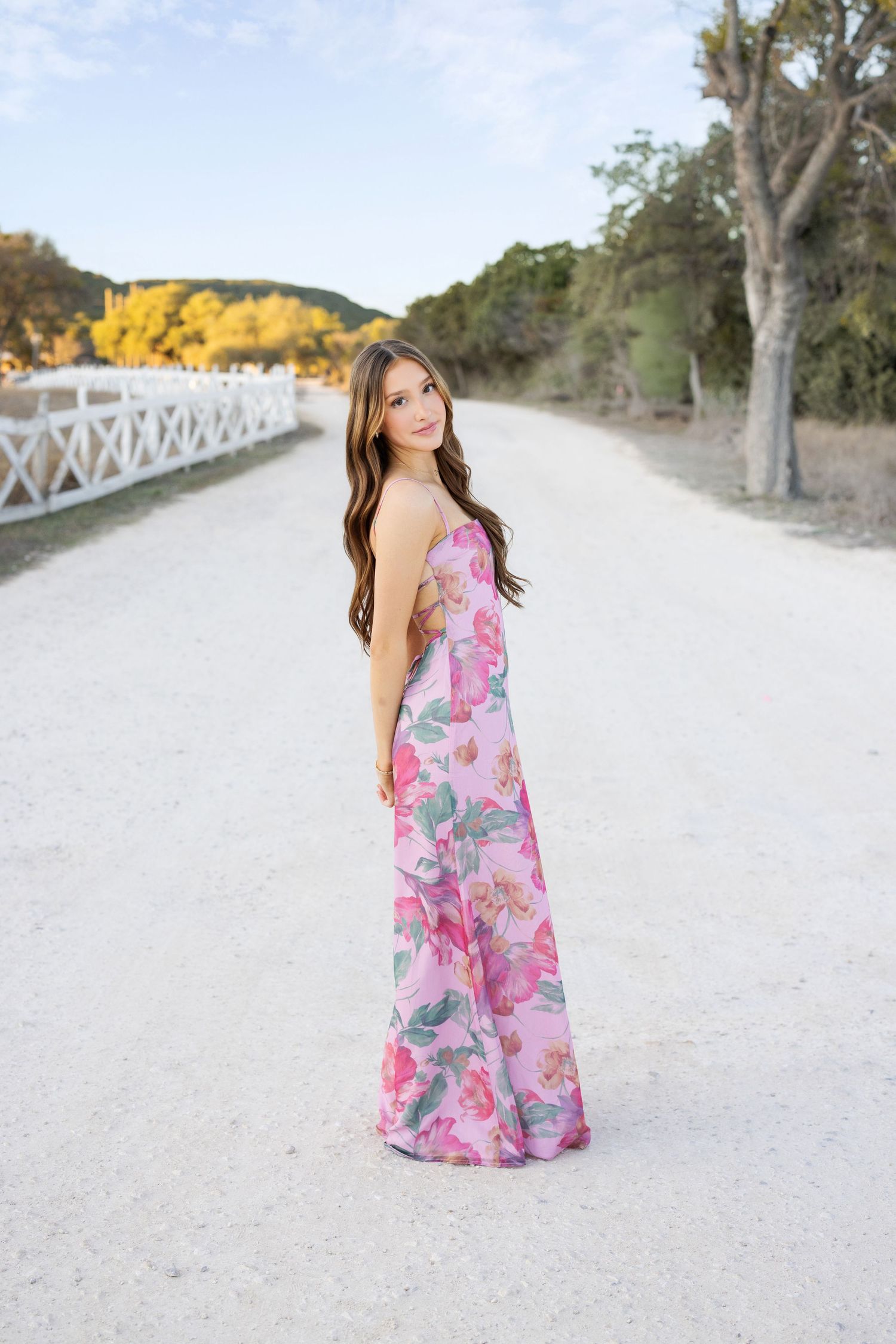 Young woman with long curly dark hair poses outdoors in white crop top and jeans near ivy-covered wall.