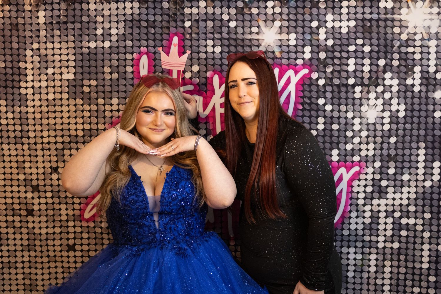 Two women posing in front of a sparkly sequin backdrop at a glamorous event.