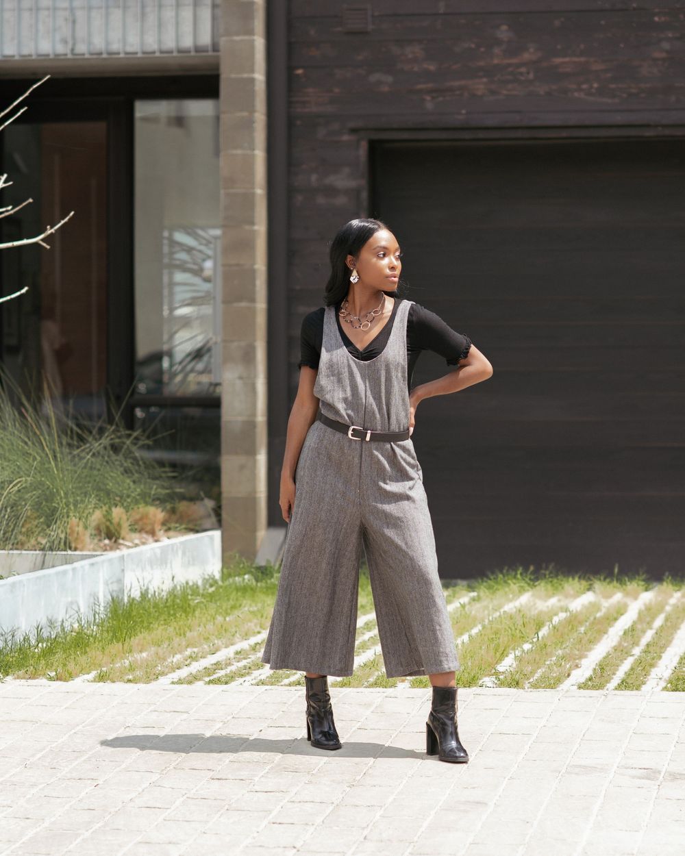 Woman in gray herringbone culottes jumpsuit with black tee and belt, styled with black ankle boots outdoors.