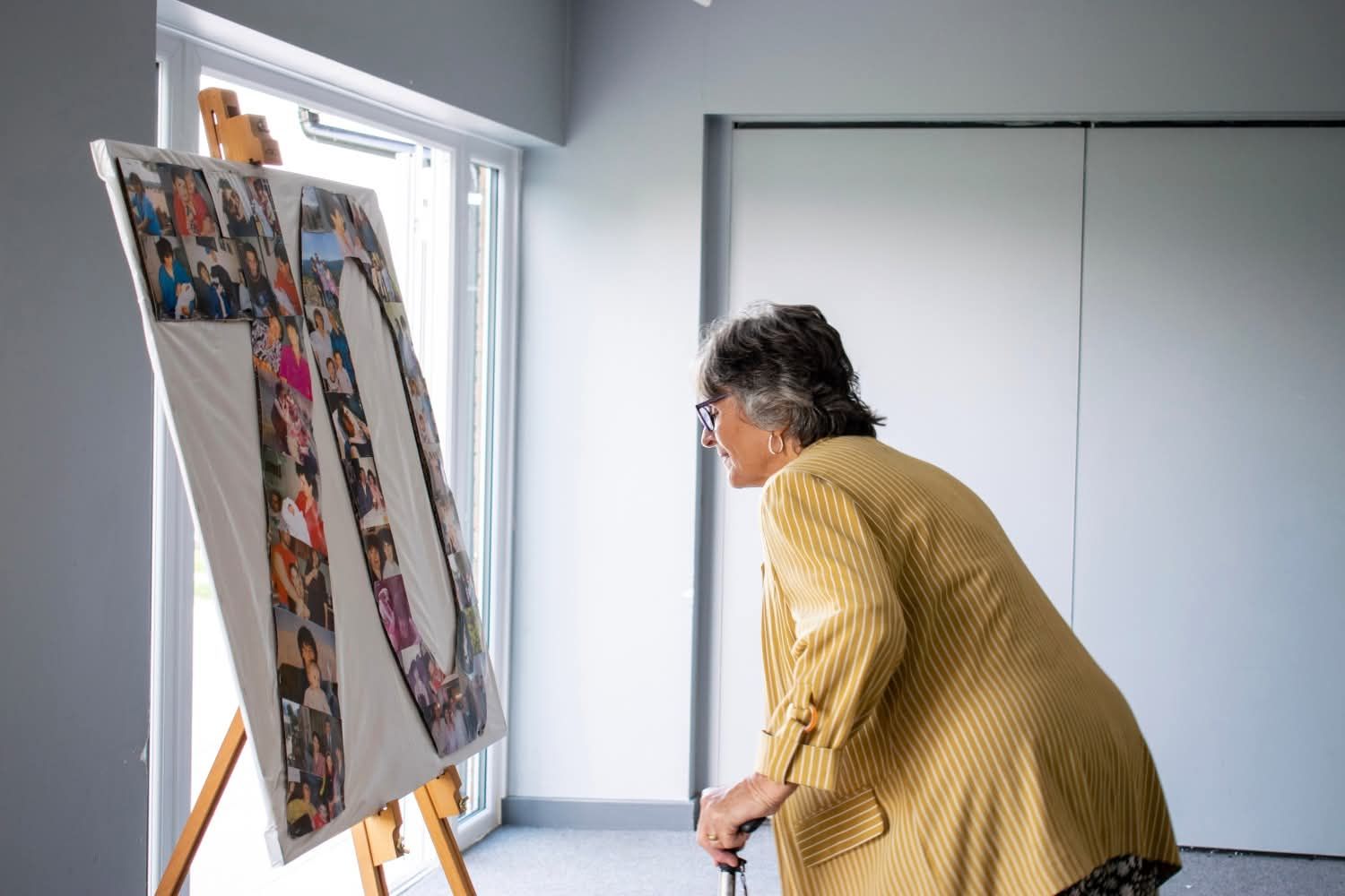 Woman in yellow jacket leaning forward to examine a photo collage display on an easel.