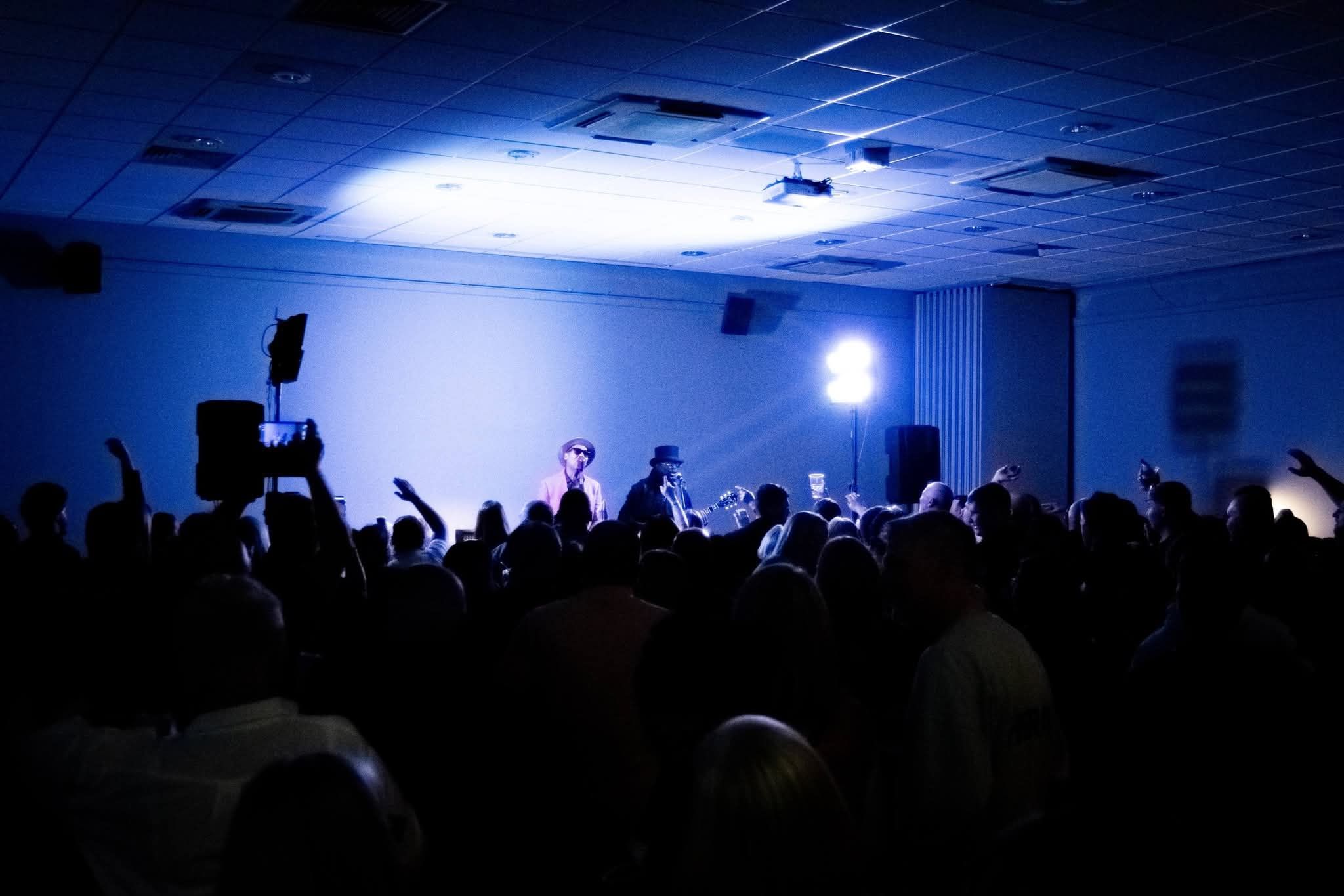Energetic concert crowd with hands raised under blue stage lighting in a venue.