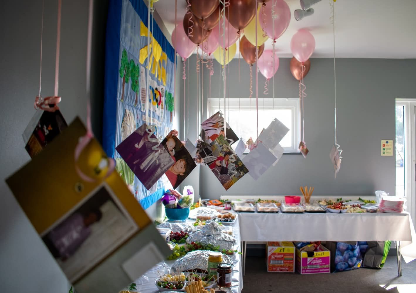 Colorful party decorations with balloons, hanging photos, and a food table at a celebration event.