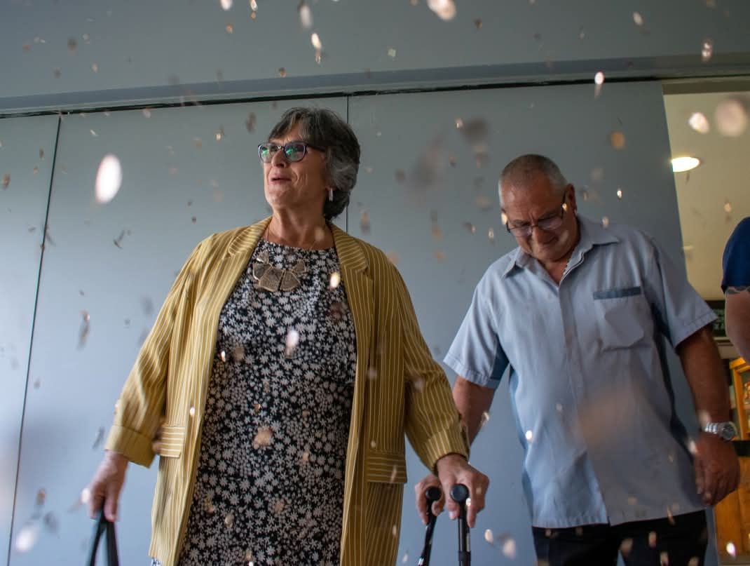 Elderly couple walking through confetti shower at a celebration event.