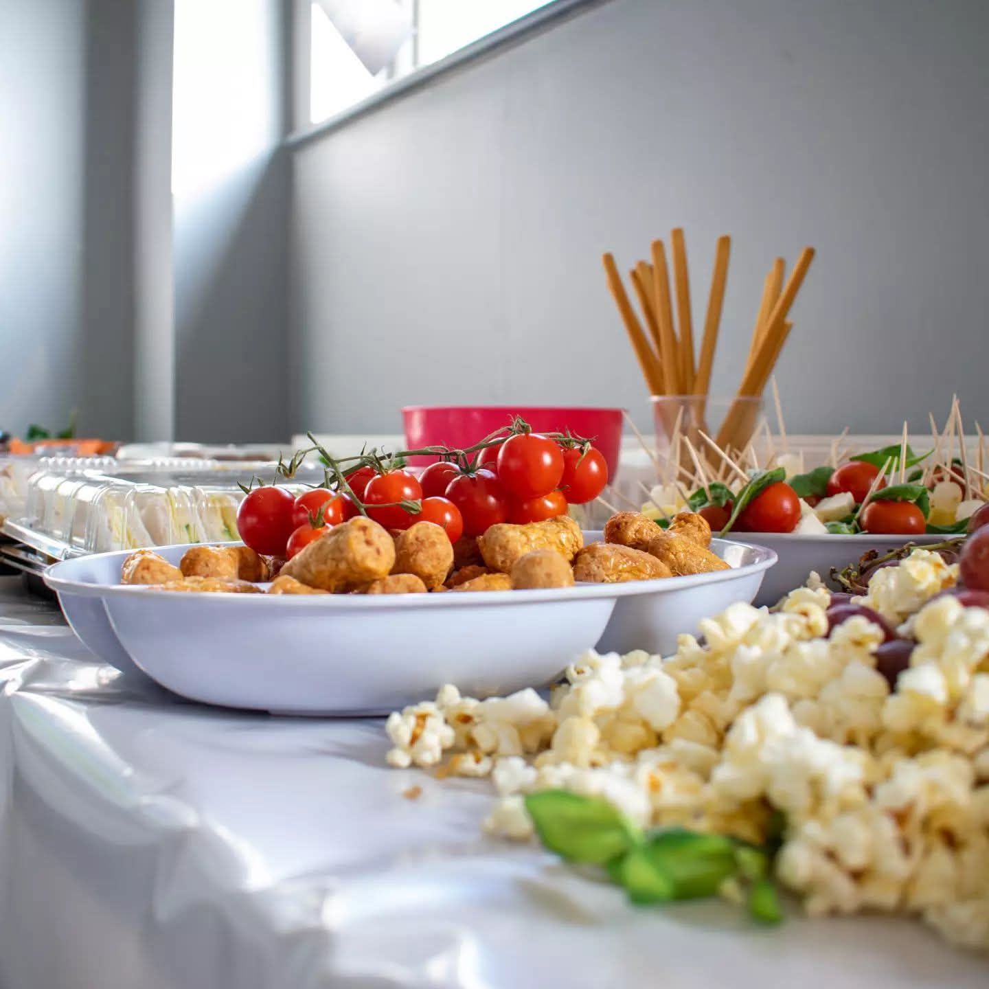 Close-up of party food spread featuring popcorn, cherry tomatoes, fried snacks, and breadsticks.