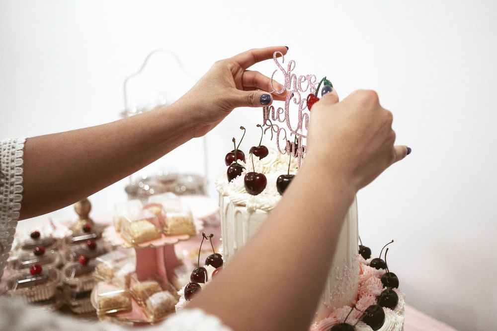 Woman placing topper on a two tier cake on the pink dessert table at a miami baby shower. It's a girl!