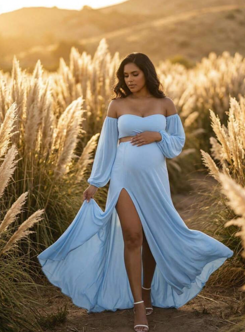 Pregnant woman in light blue off-shoulder maternity gown posing in golden pampas grass field at sunset.