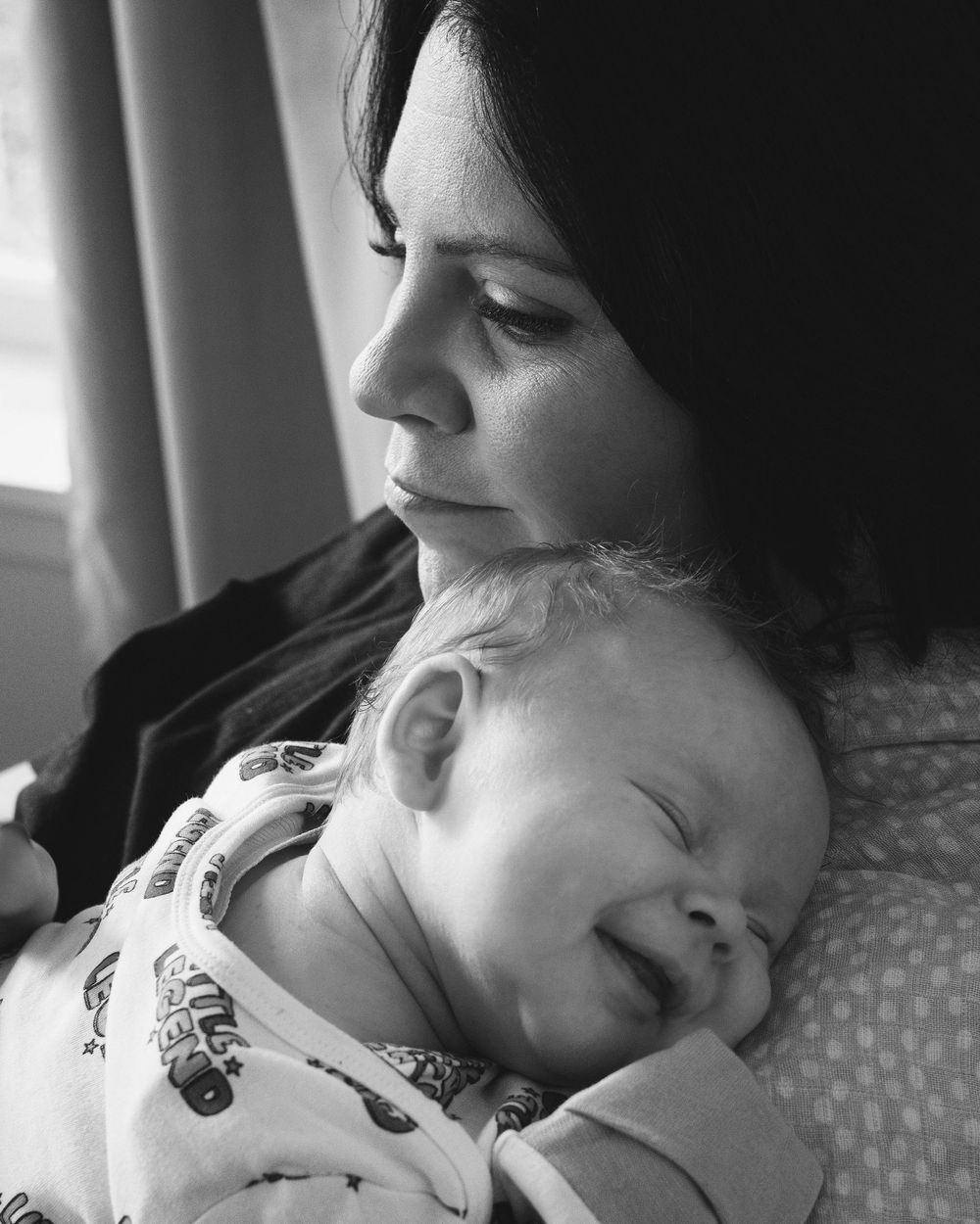 Black and white photo of a mother tenderly holding her sleeping newborn baby close to her chest.