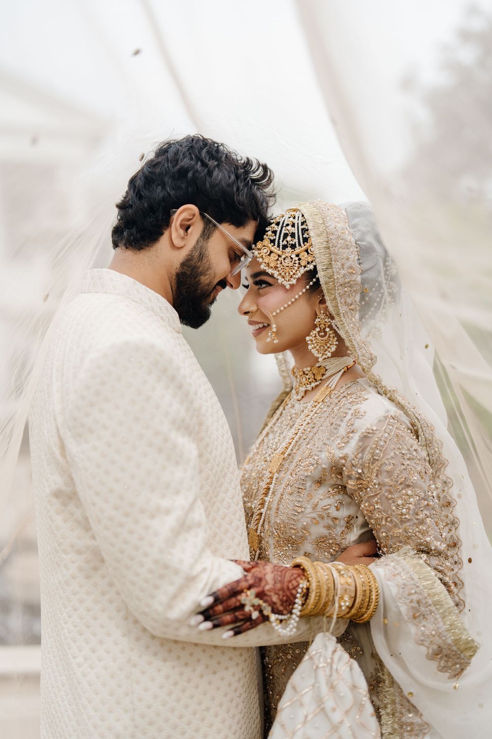 South Asian bride and groom in white and gold traditional wedding attire share an intimate moment together.