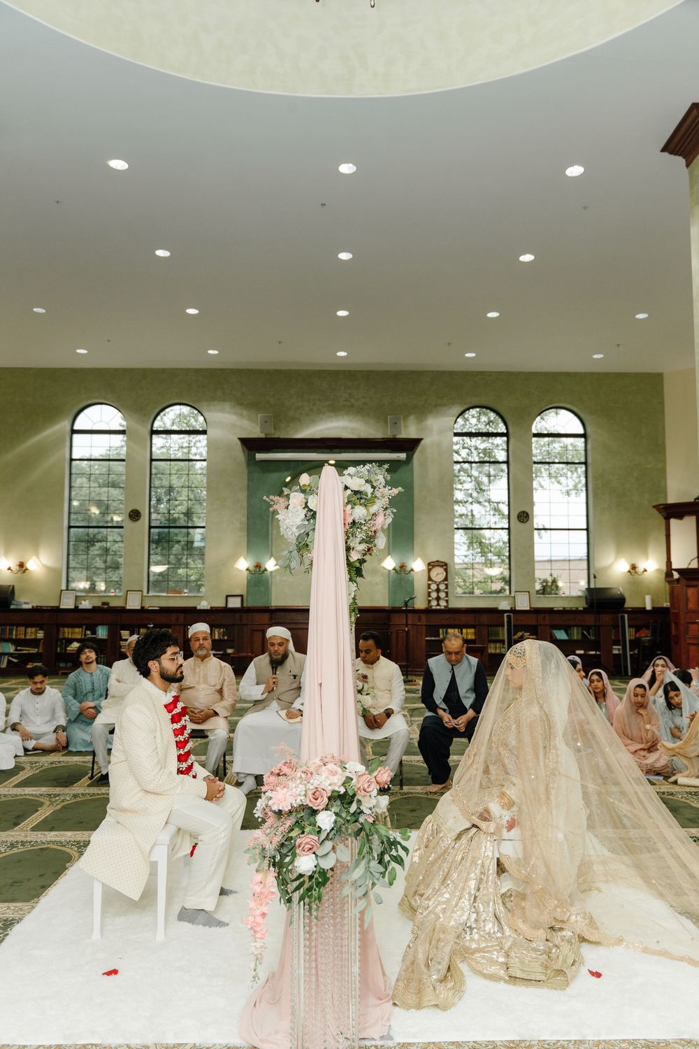 Muslim wedding ceremony with bride and groom seated during Nikah in a beautiful mosque interior.