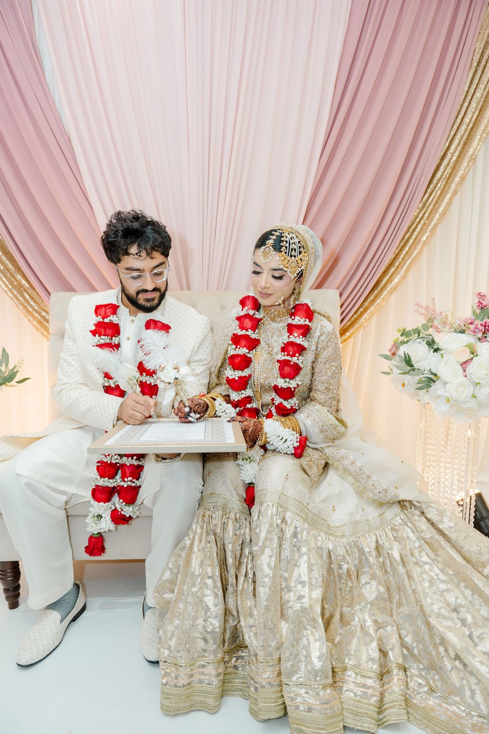 South Asian bride and groom in gold attire signing marriage certificate at wedding ceremony.