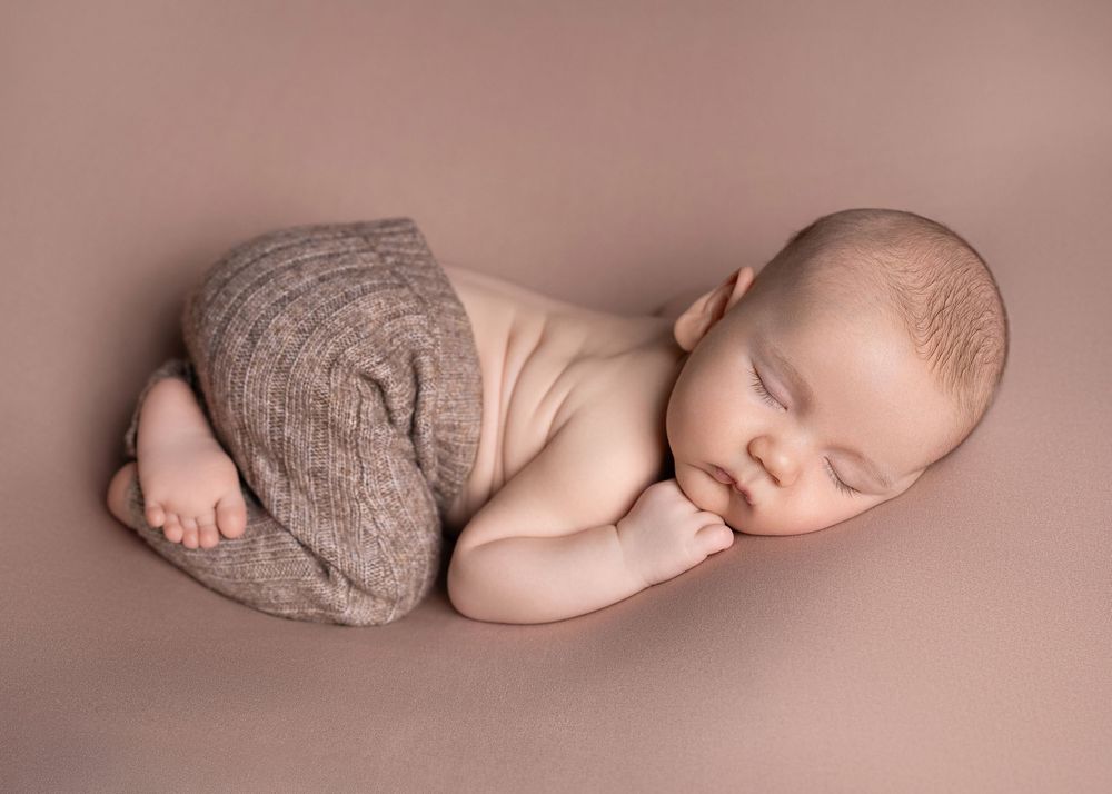 Artistic collage of seven newborn baby portraits in soft pink tones showing peaceful sleeping poses.
