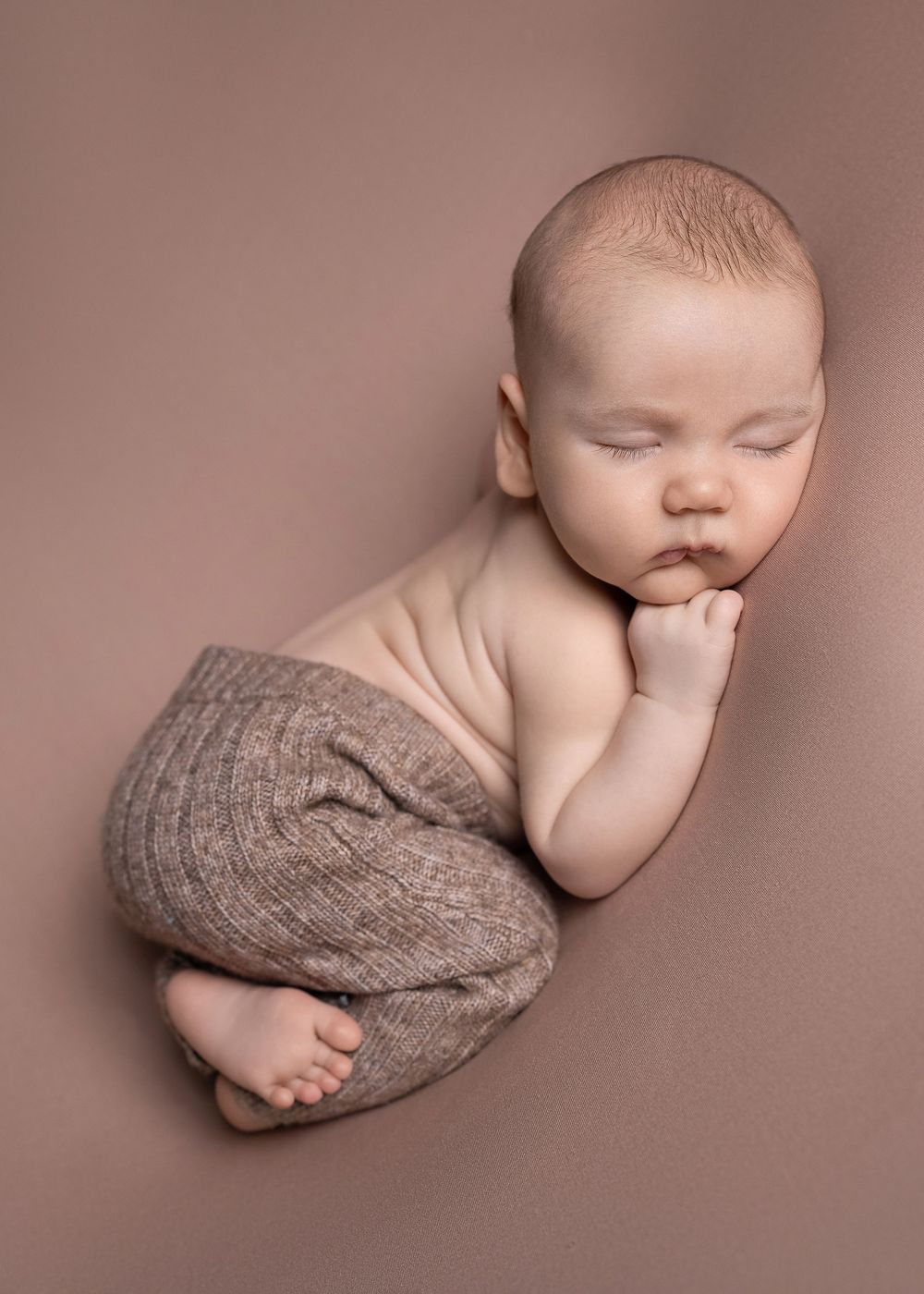 A series of artistic newborn baby photos showing gentle curled poses with soft gray knit wraps against a neutral backdrop.