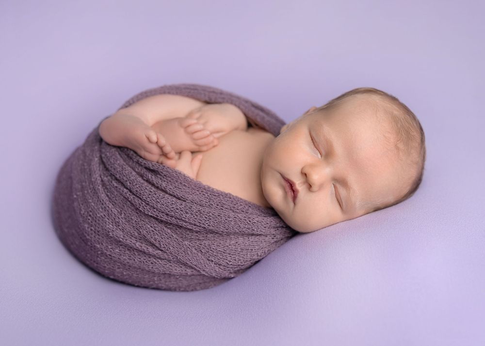 A series of six peaceful newborn baby portraits showing different angles while wrapped in a purple blanket.