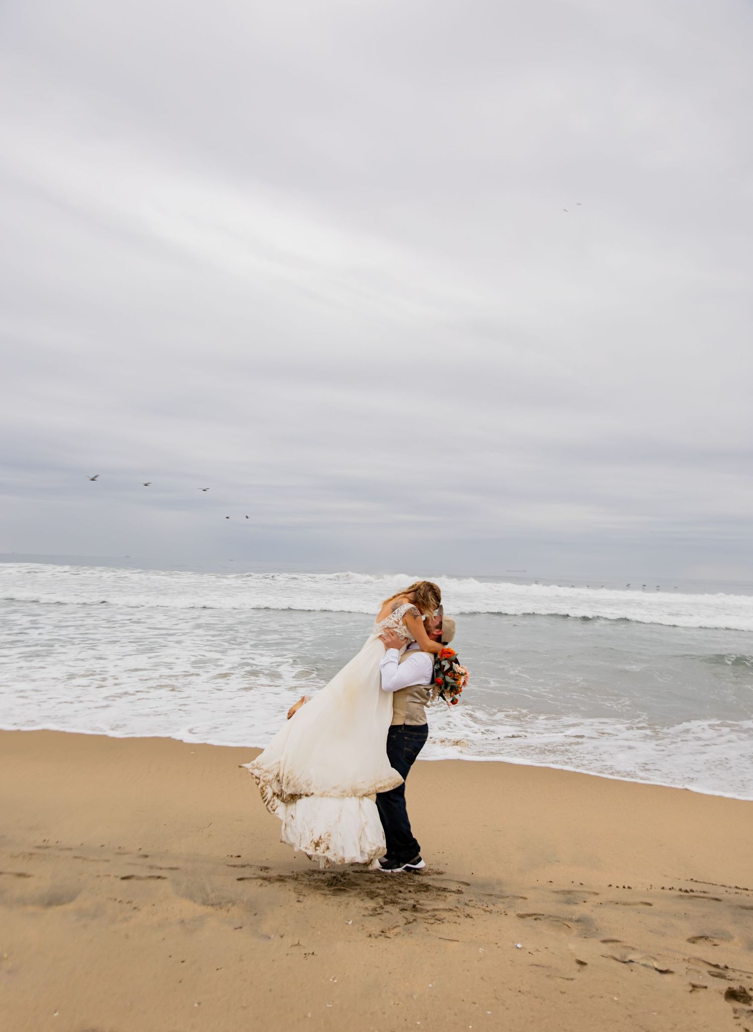A couple embraces on a misty beach with crashing waves and overcast skies in the background.
