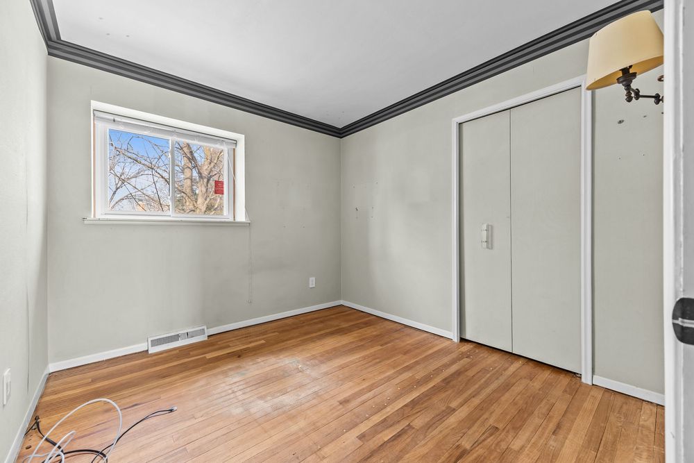 Empty bedroom with hardwood floors, crown molding, closet doors, and a window with natural light.