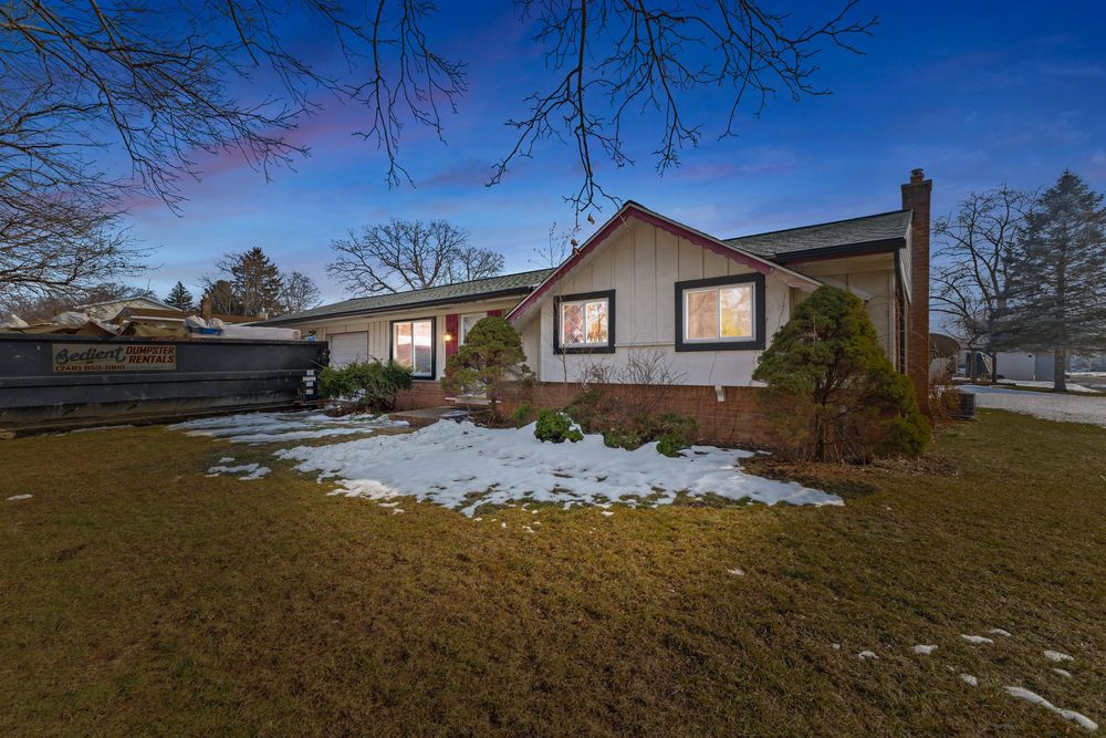 Cozy ranch home with brick exterior, chimney, and snow-patched lawn at dusk lighting.