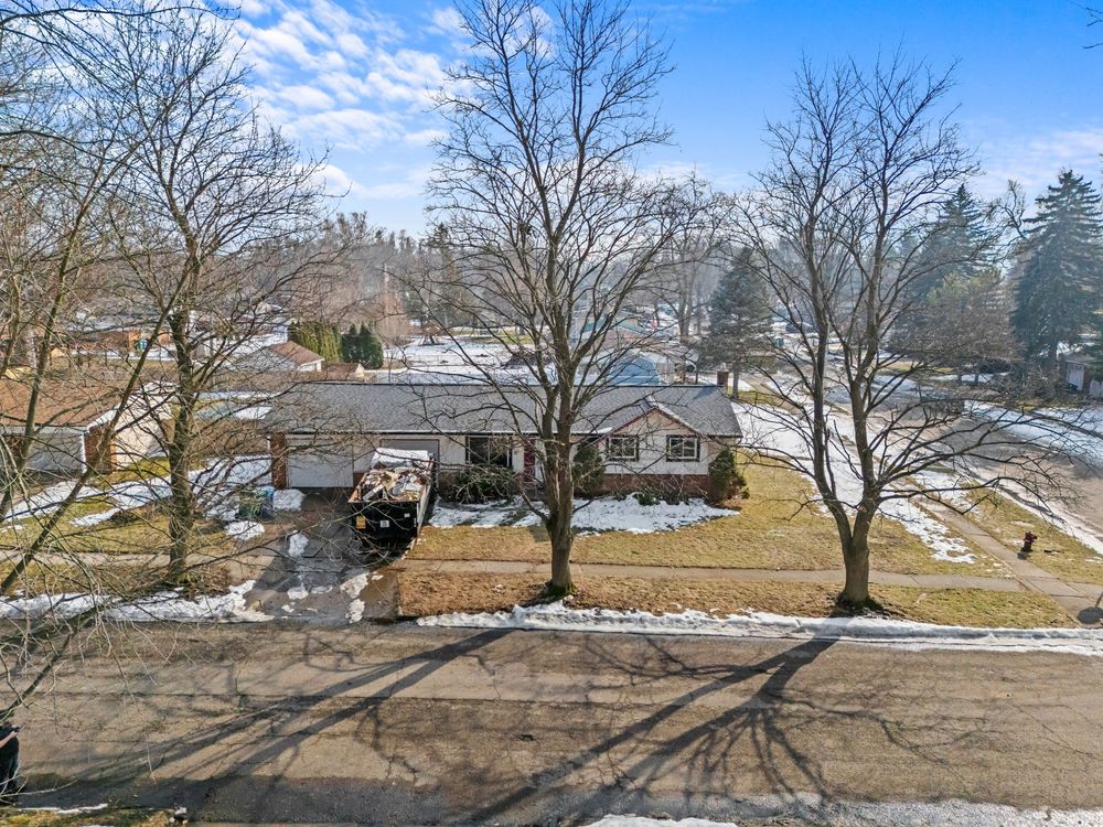 Aerial winter view of ranch home with bare trees, snow patches, and spacious yard.