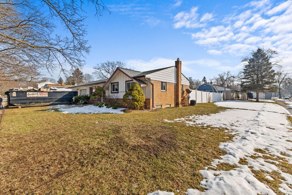 Ranch-style brick home with chimney, white fence, attached garage, and light snow on lawn.