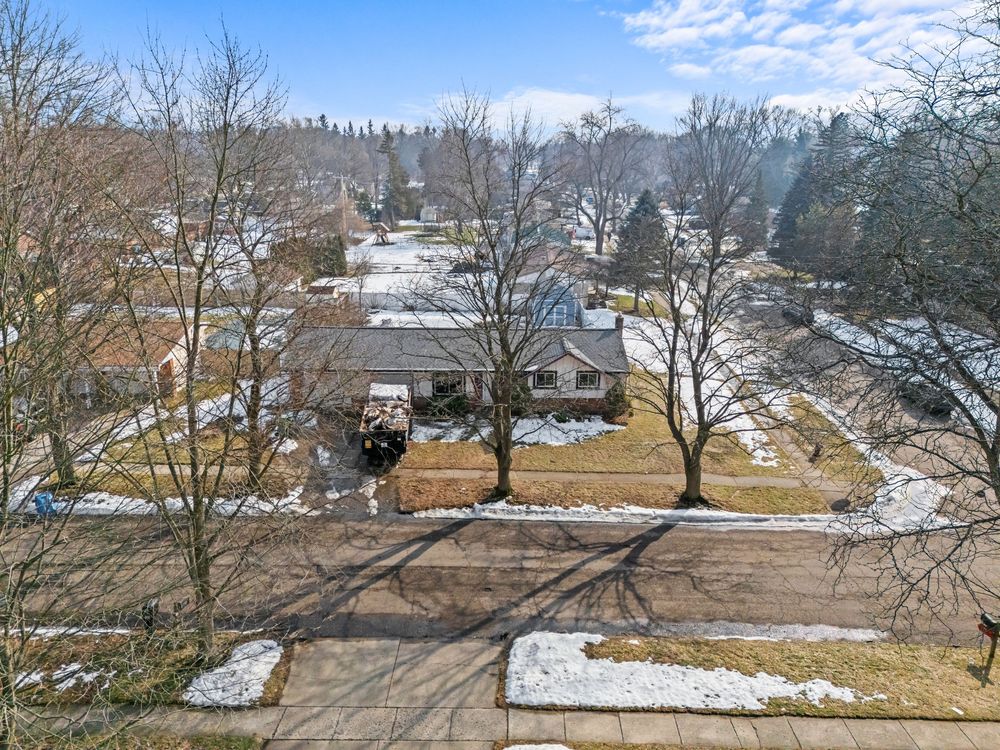 Aerial view of suburban ranch home neighborhood with bare winter trees and light snow cover.