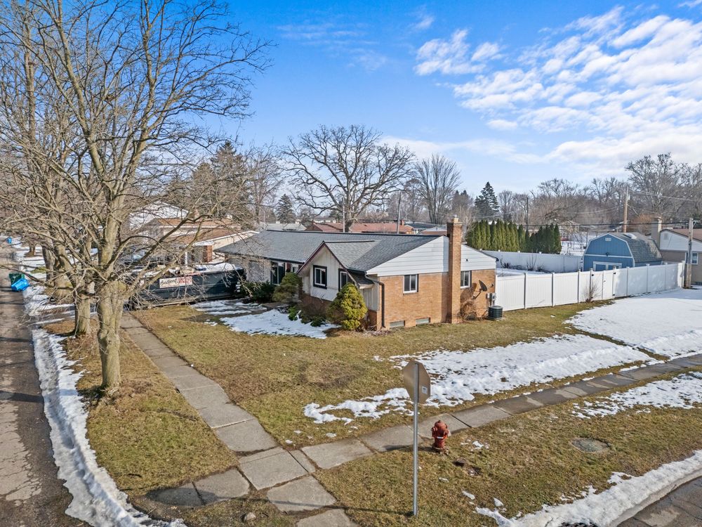 Street-level aerial view of brick ranch home with sidewalk, fire hydrant, and snowy lawn.