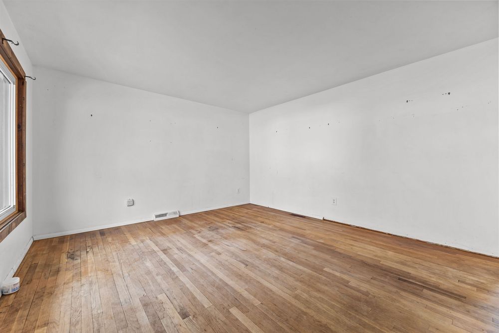 Empty bright room with hardwood floors, white walls, and natural window light.