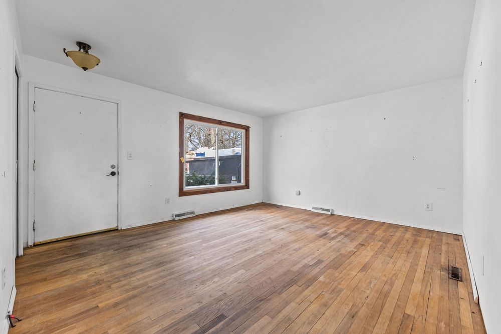 Vacant room with warm hardwood floors, white walls, and a wood-framed window.
