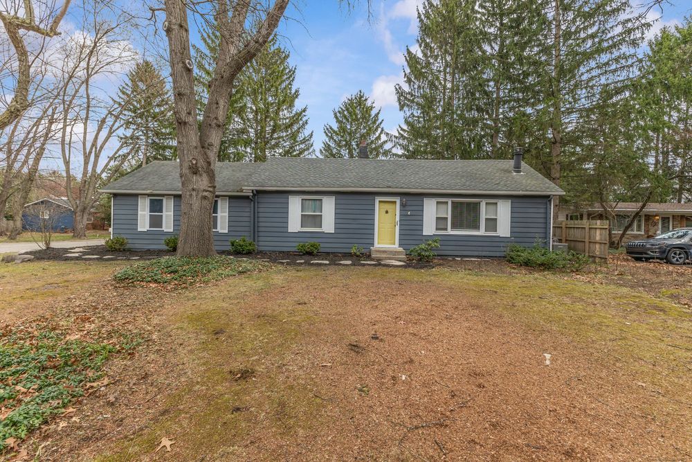 Ranch-style home with blue-gray siding, yellow front door, and large front yard.