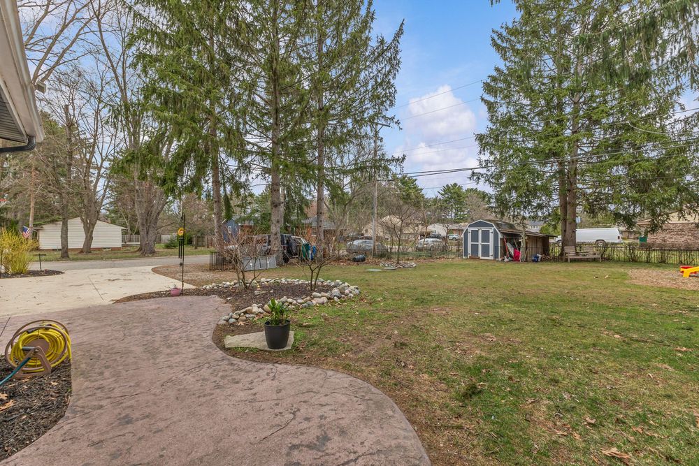 Spacious backyard with lush green lawn, tall pine trees, patio area, and a small red storage shed.