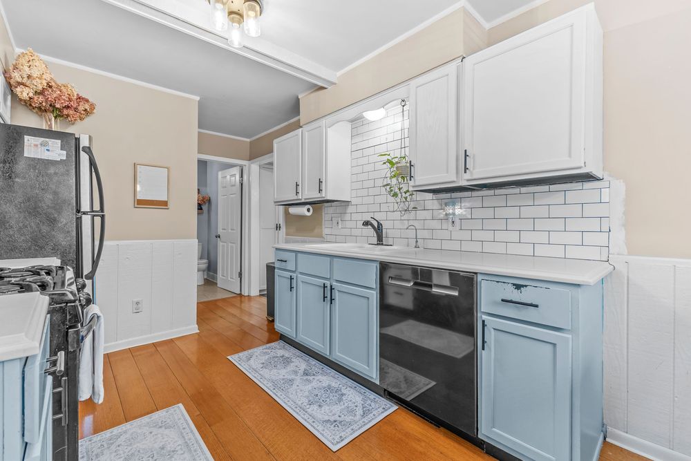 Bright kitchen featuring light blue cabinets, white subway tile backsplash, and hardwood floors.