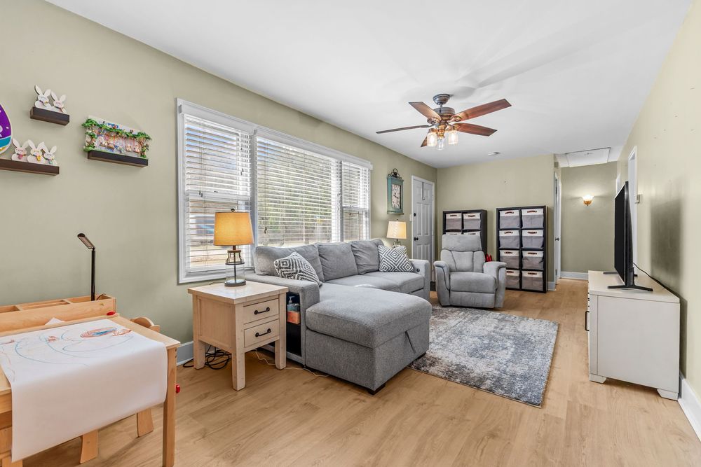 Bright living room with gray sectional sofa, ceiling fan, and light hardwood flooring.