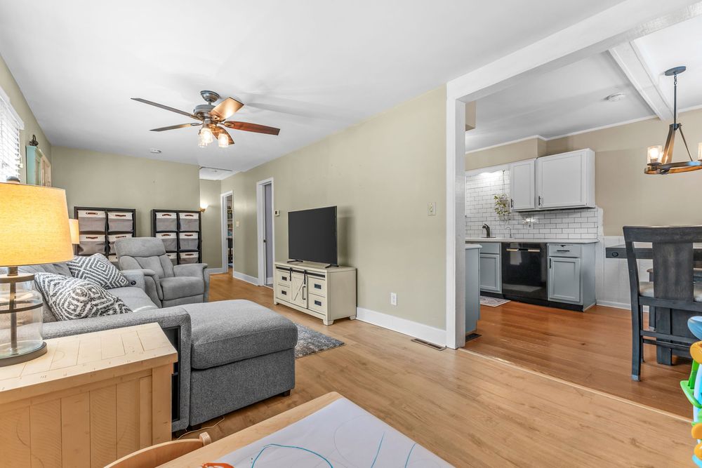 Open-concept living room with gray sofa, ceiling fan, and view into updated kitchen beyond.