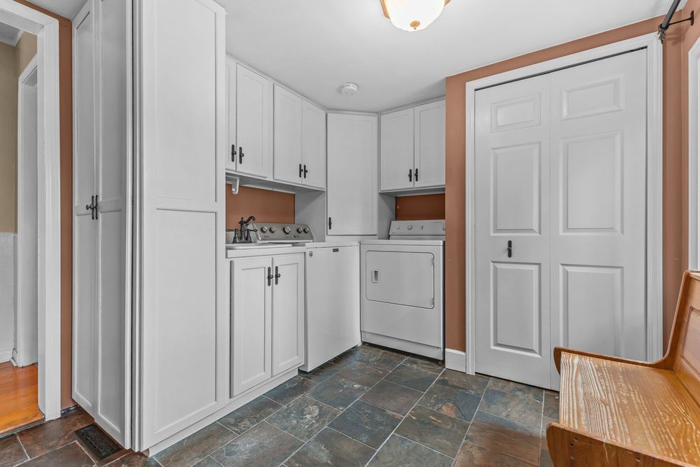 White kitchen laundry area with upper cabinets, washer, and dark slate tile flooring.