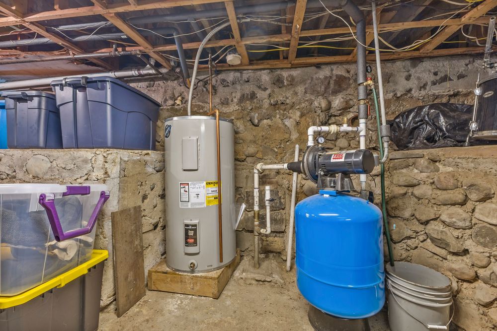 Basement utility room with electric water heater, blue pressure tank, and stone foundation walls.
