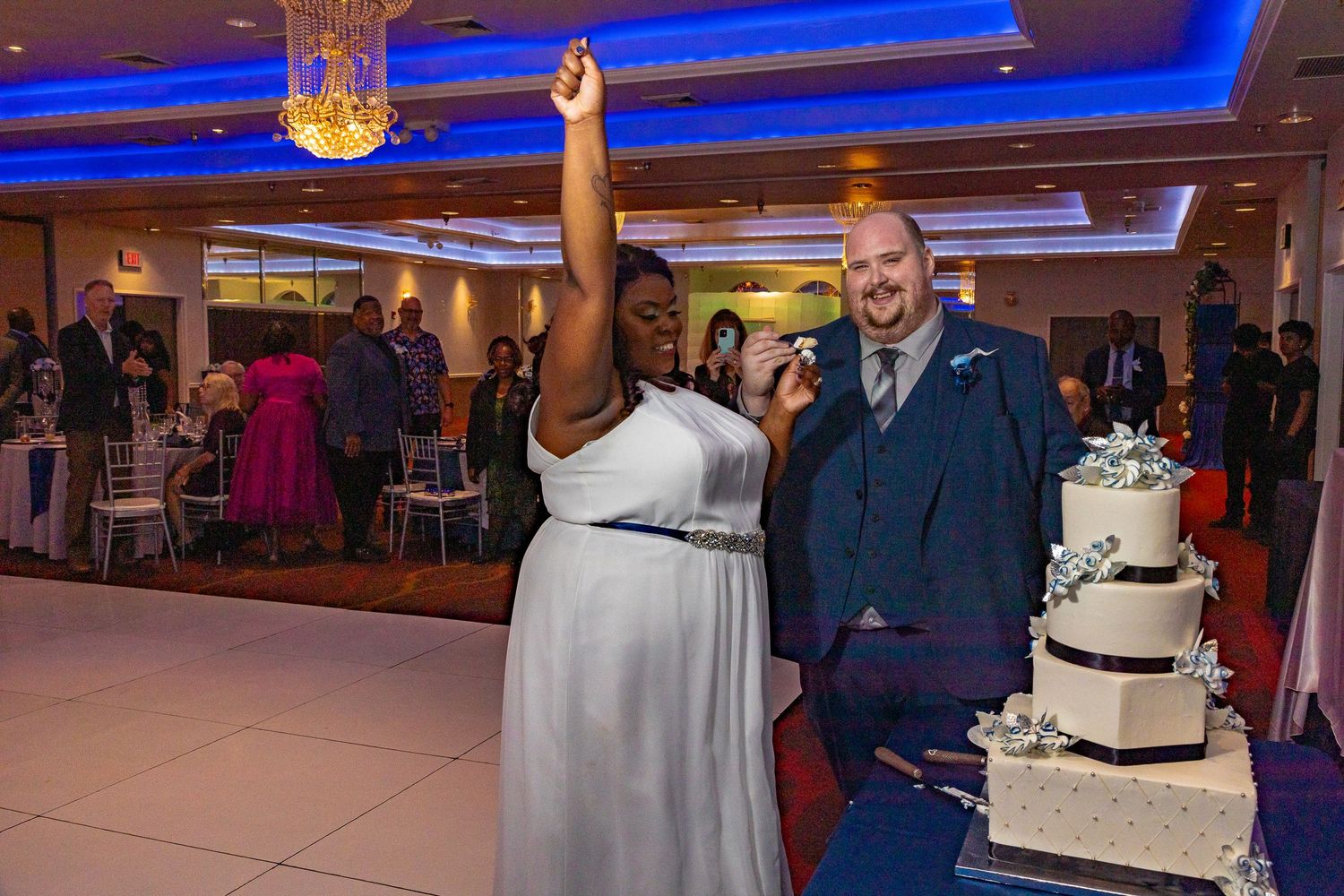 Bride and groom cutting wedding cake at elegant reception venue with blue lighting.