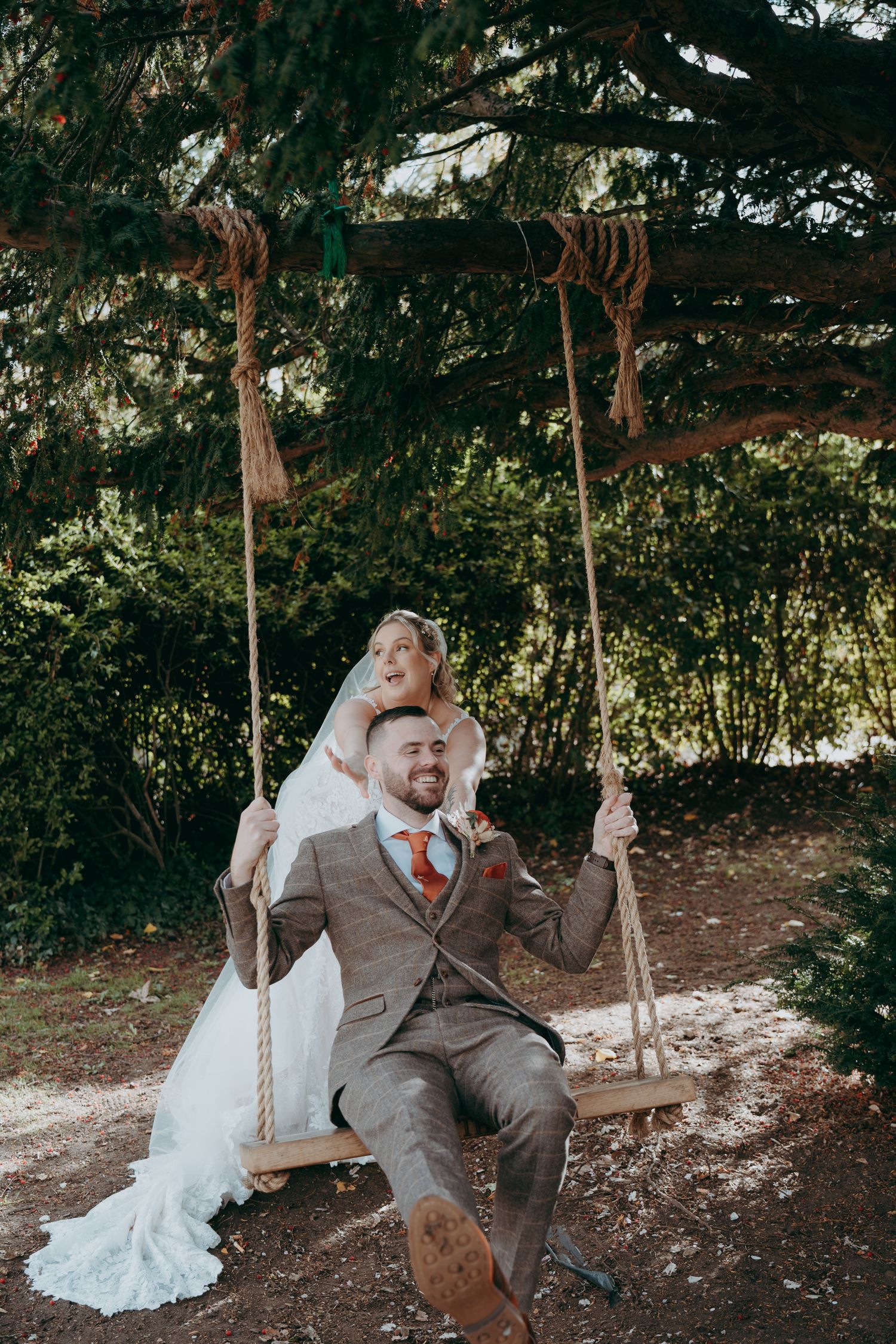 Bride in white off-shoulder gown and groom in black tuxedo holding champagne in a rustic barn venue.