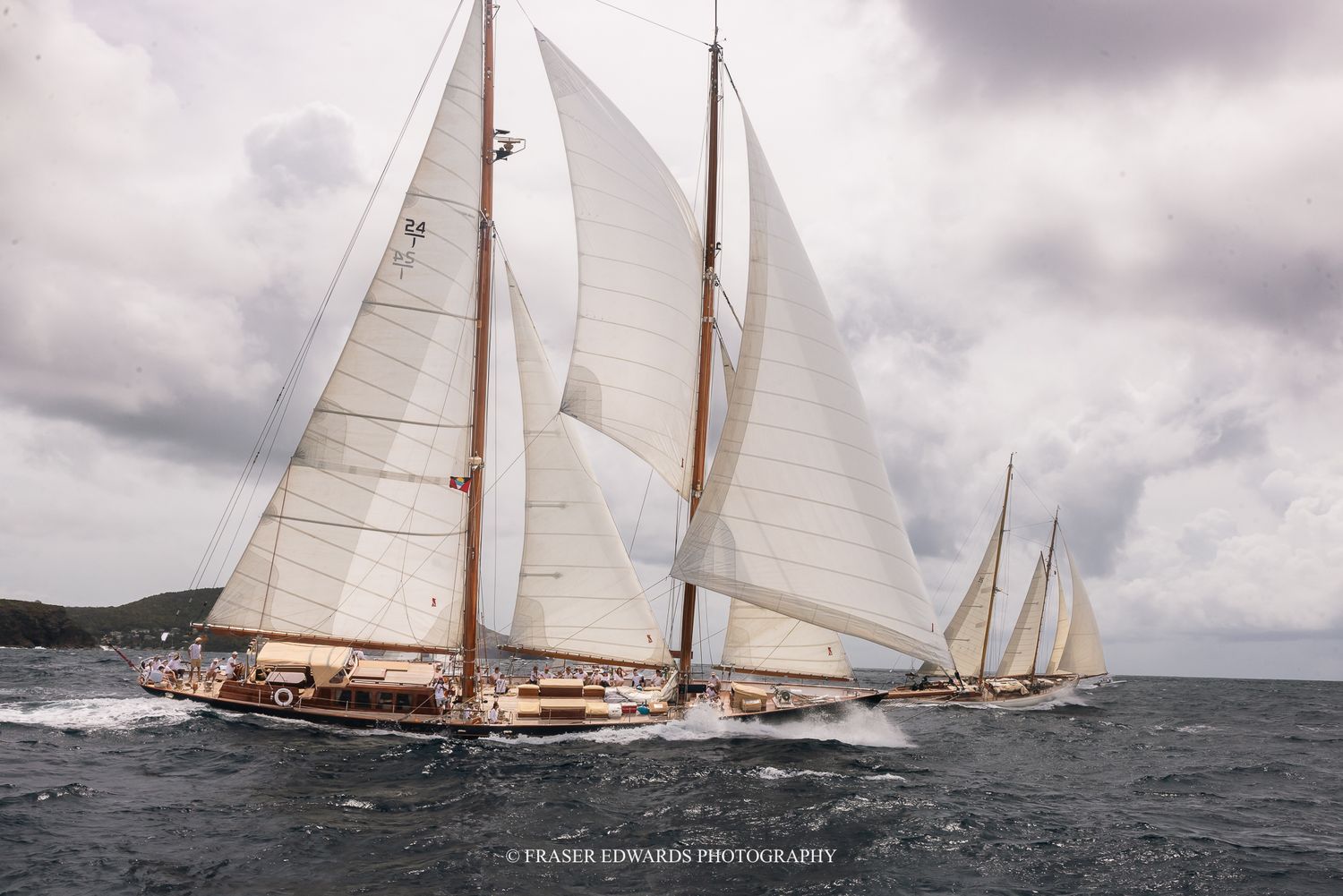 Classic tall sailing yachts with white sails race across choppy waters under overcast skies in a stunning regatta.