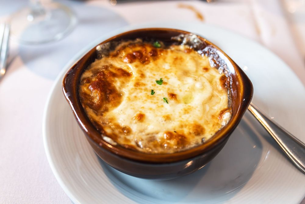 Golden-brown French onion soup topped with melted cheese crust served in a rustic ceramic bowl on white plate.