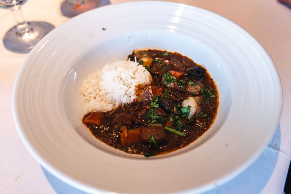 A bowl of rich dark curry with white rice, mushrooms, and greens served in a white ceramic bowl.