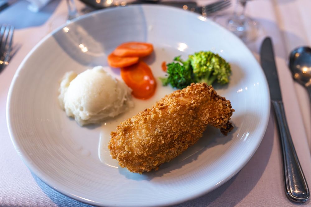 Breaded chicken Kiev served with mashed potatoes, glazed carrots, and steamed broccoli on a white plate.