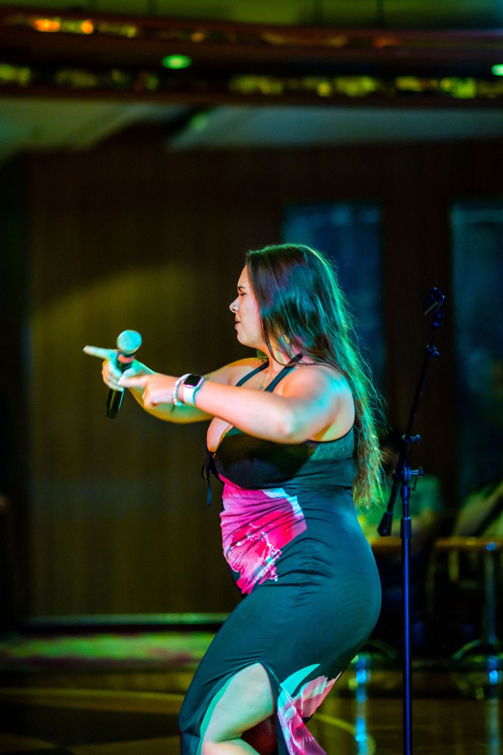 Woman performer singing on stage, holding microphone, wearing black outfit under colorful stage lighting.