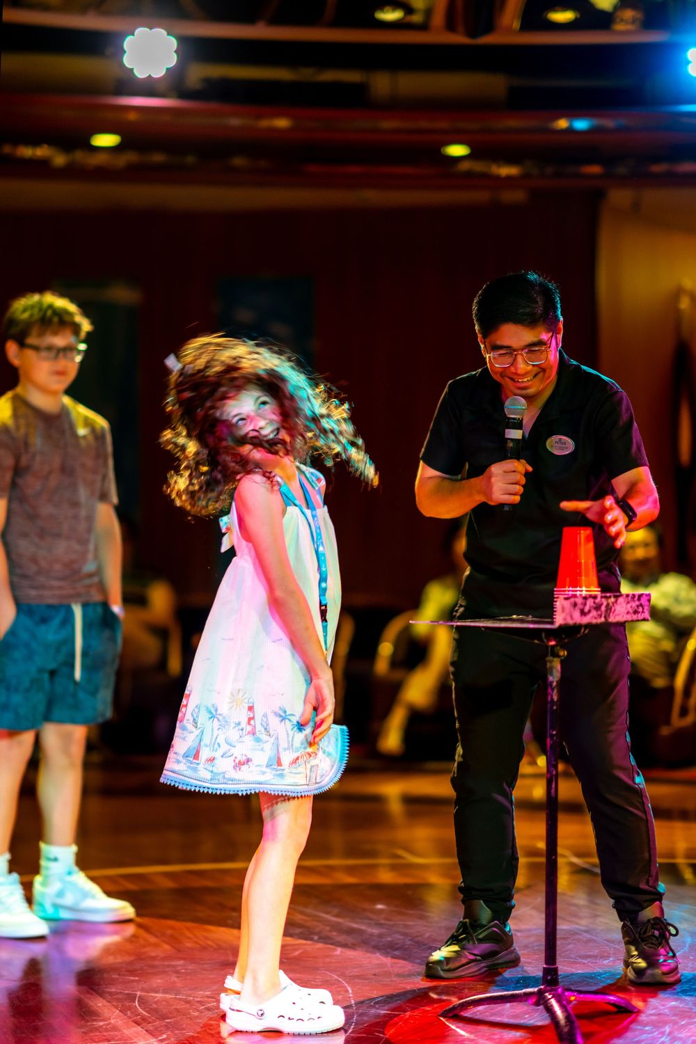 A young girl spins on stage while a smiling host holds a microphone during a children's talent show performance.