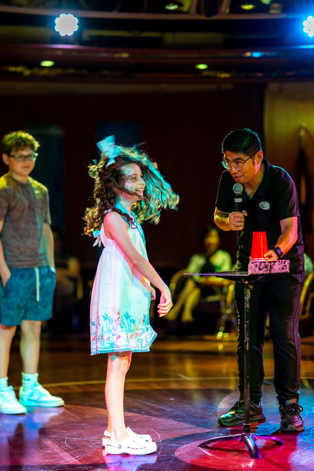 Young girl spinning on stage during a magic show performance, with a magician holding a microphone nearby.
