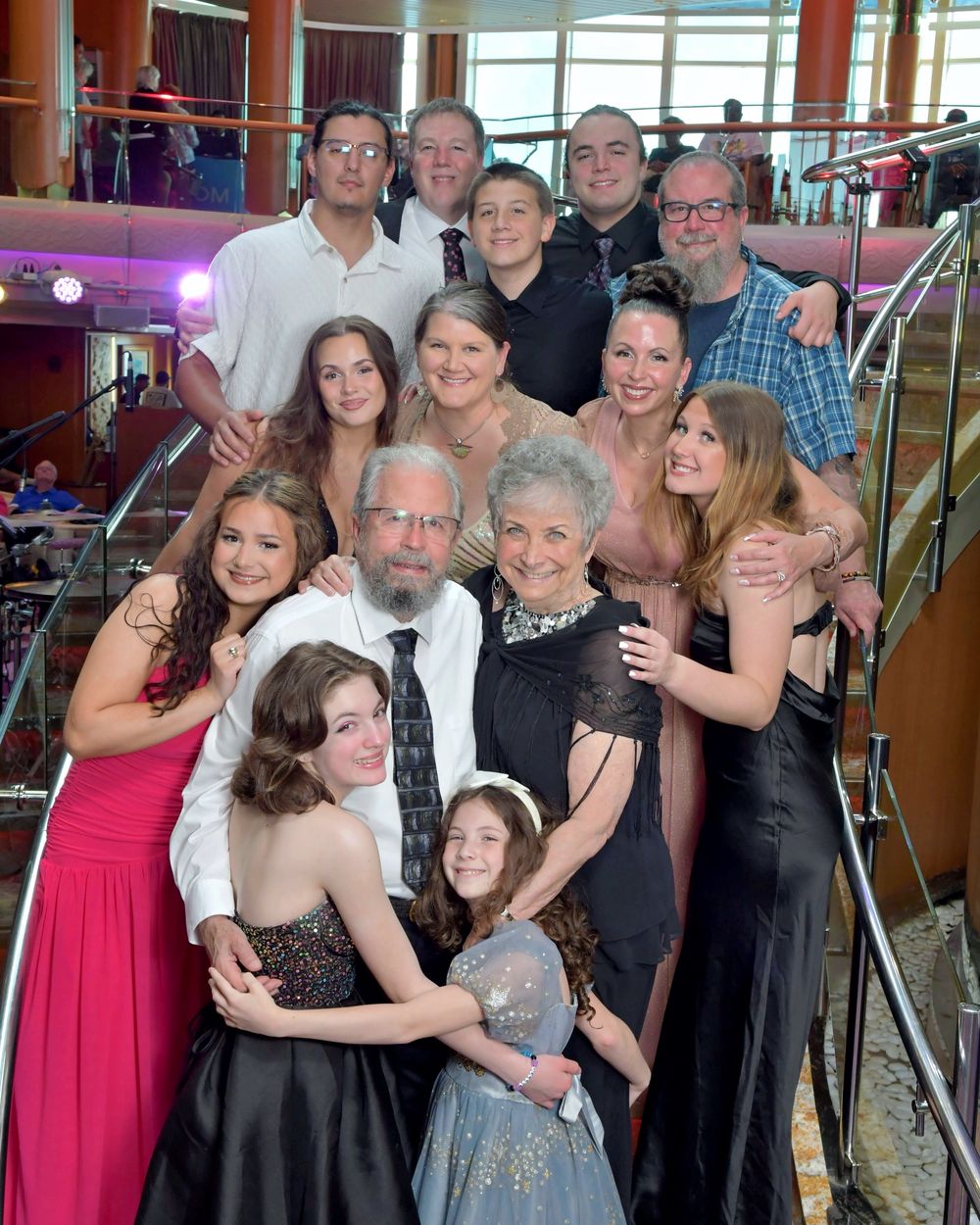 Large multigenerational family group photo on cruise ship staircase, dressed in formal evening attire, smiling together.